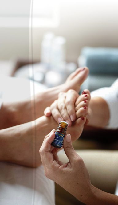 Hände geben eine Fußmassage mit ätherischem Öl an einem entspannten Fuß.