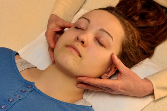 Therapeutin hält Kiefer einer liegenden Frau.