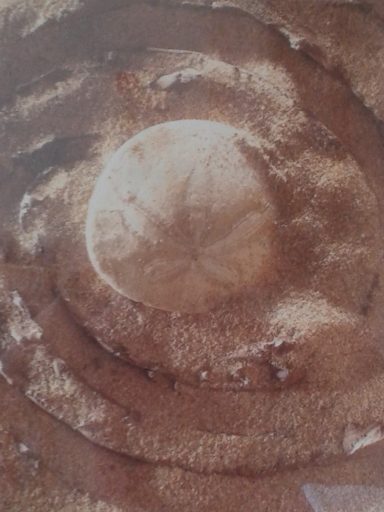 Sandmuster mit einer runden Vertiefung in der Mitte und spiralförmigen Linien.